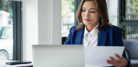 Woman in an office reviewing documents while working on a laptop at her desk
