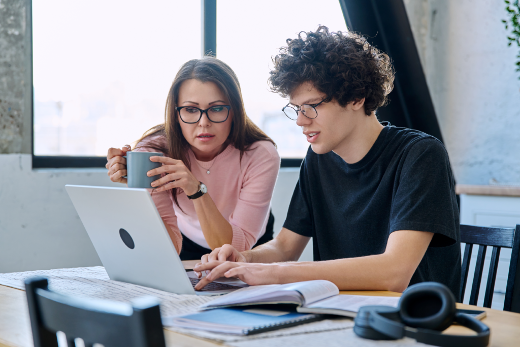 Parent and student reviewing information together on a laptop at a table with books and notes
