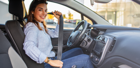 Woman sitting in the driver’s seat fastening her seatbelt inside a car