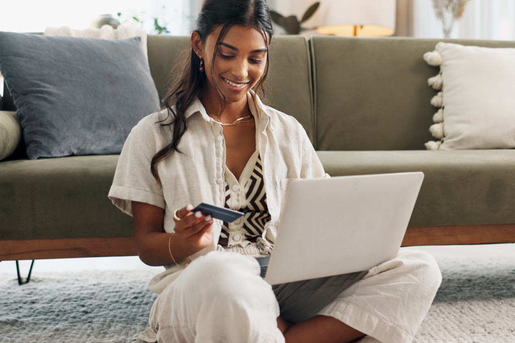 Person sitting on the floor using a laptop while holding a credit card at home.