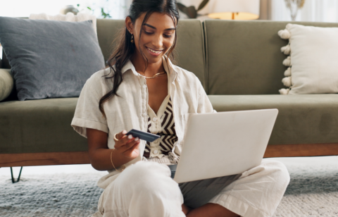Person sitting on the floor using a laptop while holding a credit card at home.