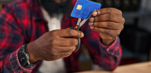 Person using scissors to cut a credit card while sitting at a desk.