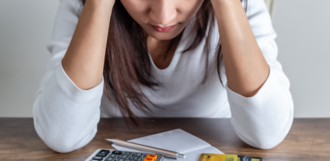 Person holding their head while looking down at a calculator, receipt, and credit cards on a table.