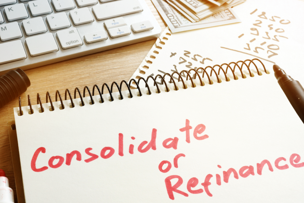 Notebook with the words “Consolidate or Refinance” written in red marker, next to a calculator, keyboard, and cash on a desk.