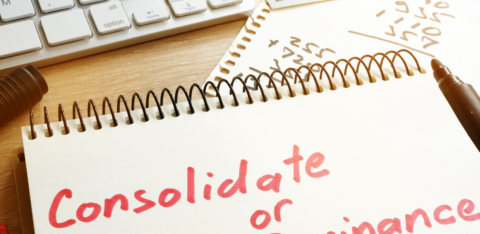 Notebook with the words “Consolidate or Refinance” written in red marker, next to a calculator, keyboard, and cash on a desk.