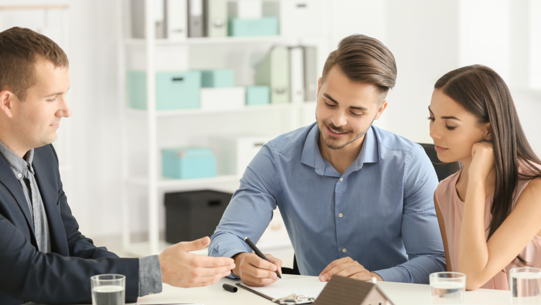 Couple signing paperwork with a professional at a desk, with a small house model in front
