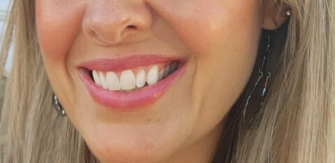 Close-up portrait of a smiling woman with long blonde hair outdoors.
