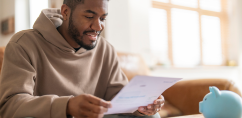 Man sitting at a table reviewing a document with a piggy bank nearby.