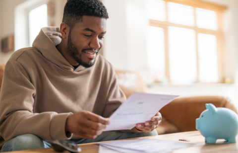 Man sitting at a table reviewing a document with a piggy bank nearby.