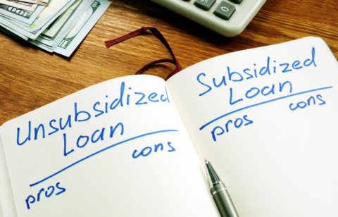 Notebook comparing unsubsidized and subsidized loans with pros and cons, next to cash and a calculator