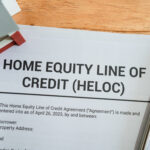 Document titled “Home Equity Line of Credit (HELOC)” on a desk with a pen and small house model nearby.