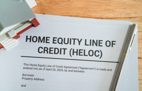 Document titled “Home Equity Line of Credit (HELOC)” on a desk with a pen and small house model nearby.