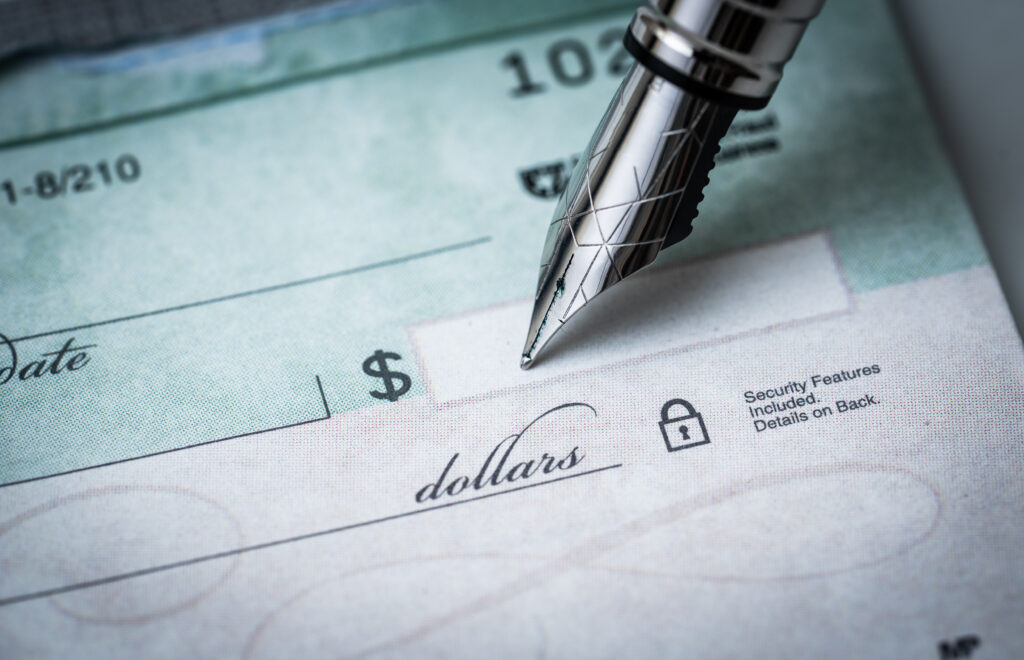 Close-up of a pen writing on a blank check with the dollar amount line visible.