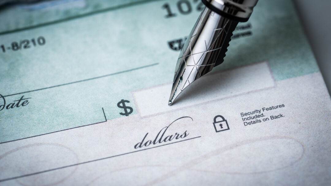 Close-up of a pen writing on a blank check with the dollar amount line visible.