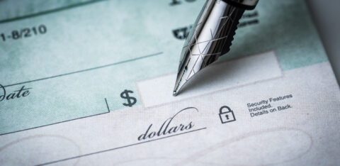 Close-up of a pen writing on a blank check with the dollar amount line visible.
