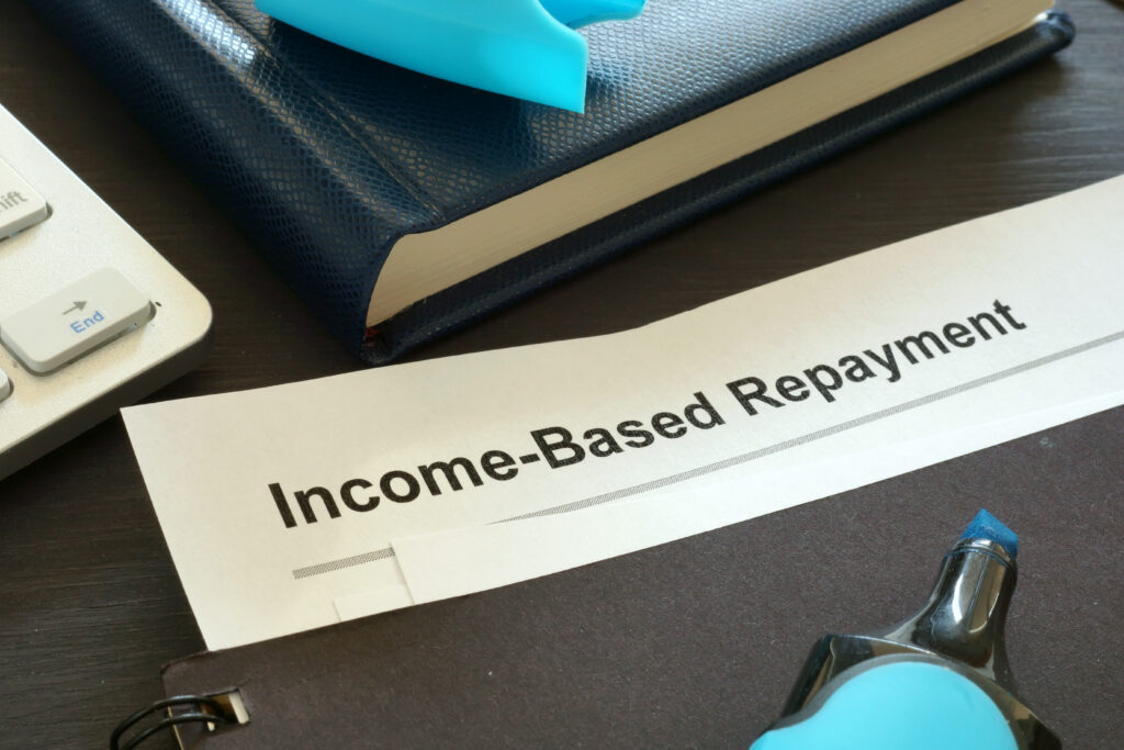 Close-up of a document labeled “Income-Based Repayment” on a desk with a notebook, keyboard, and office supplies.