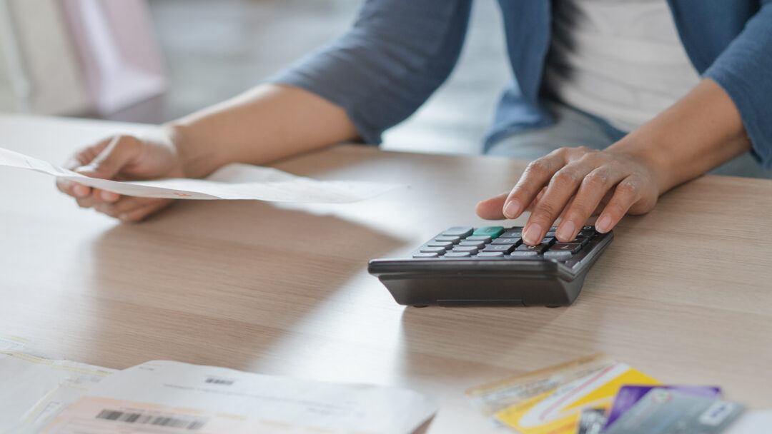 Person using a calculator while reviewing bills and holding a document at a desk.