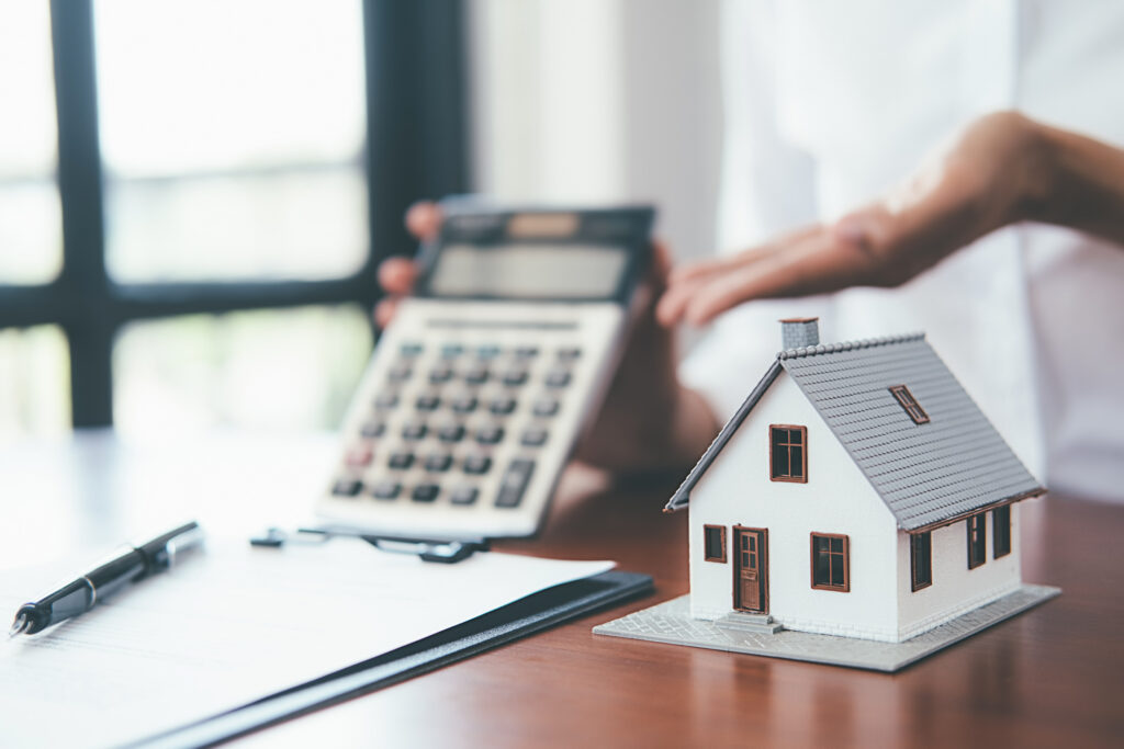 Small model house on a desk with a calculator and paperwork in the background.