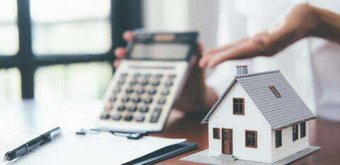 Small model house on a desk with a calculator and paperwork in the background.