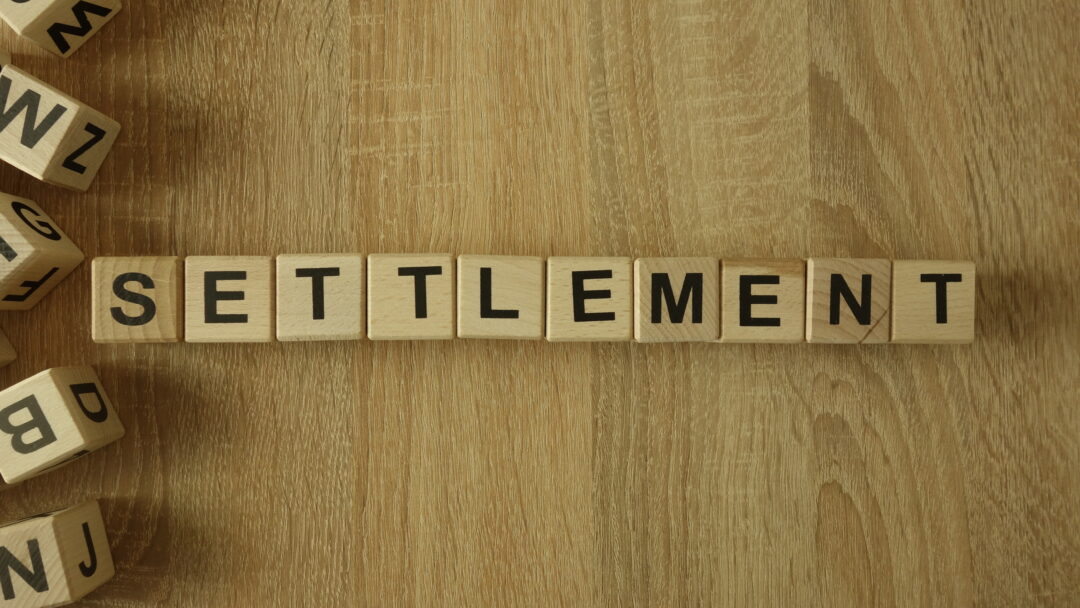 Wooden letter tiles spelling “SETTLEMENT” arranged on a wood surface.