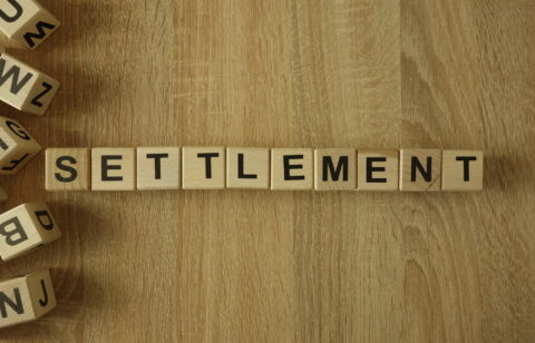 Wooden letter tiles spelling “SETTLEMENT” arranged on a wood surface.