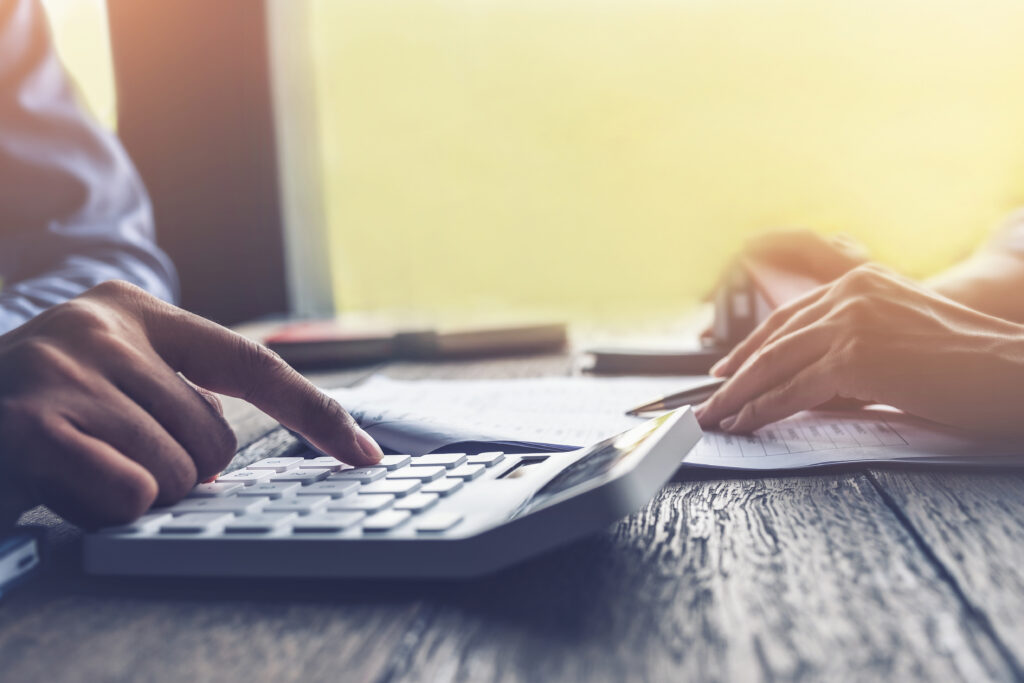 Close-up of hands using a calculator while reviewing paperwork on a desk.