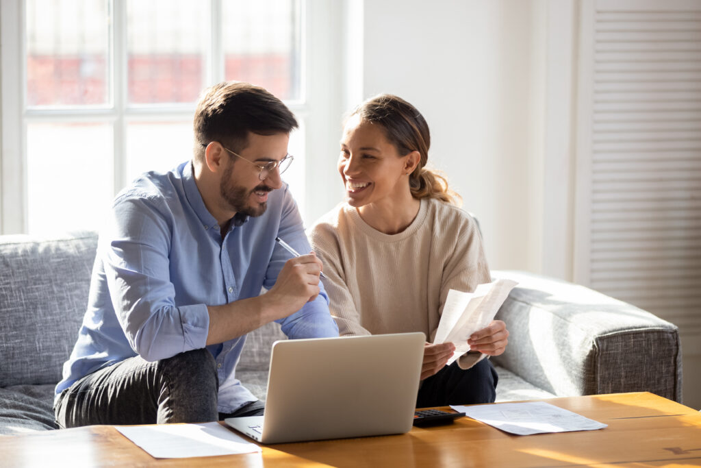 Couple sitting on a couch reviewing bills and using a laptop together.
