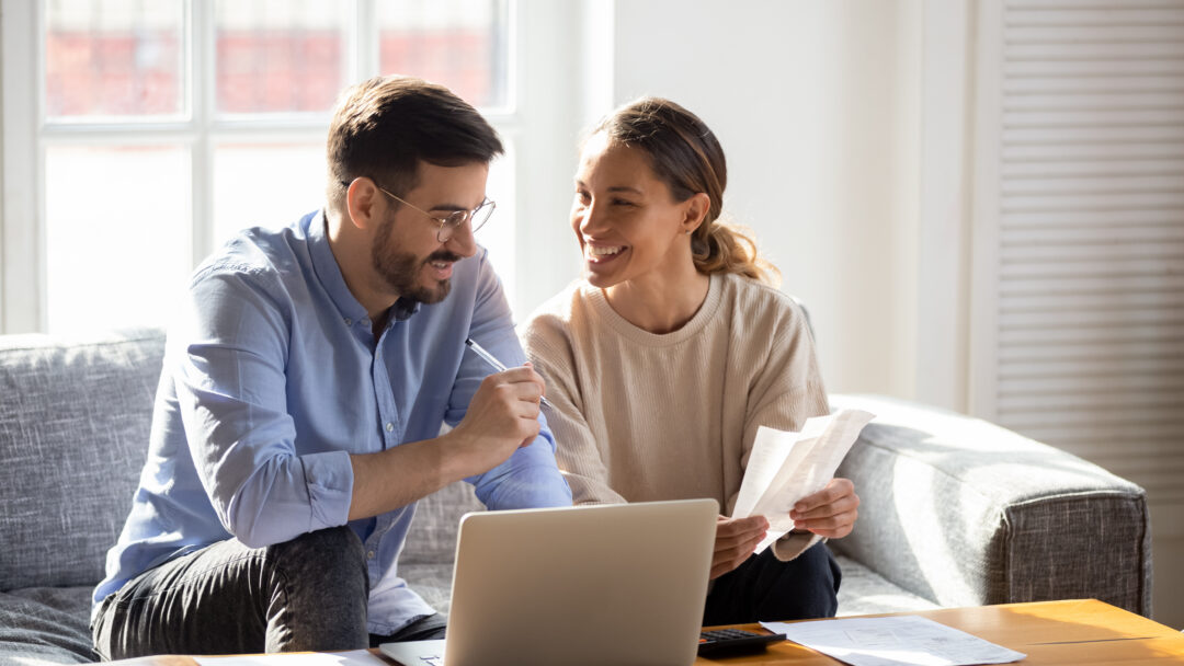 Couple sitting on a couch reviewing bills and using a laptop together.