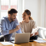 Couple sitting on a couch reviewing bills and using a laptop together.