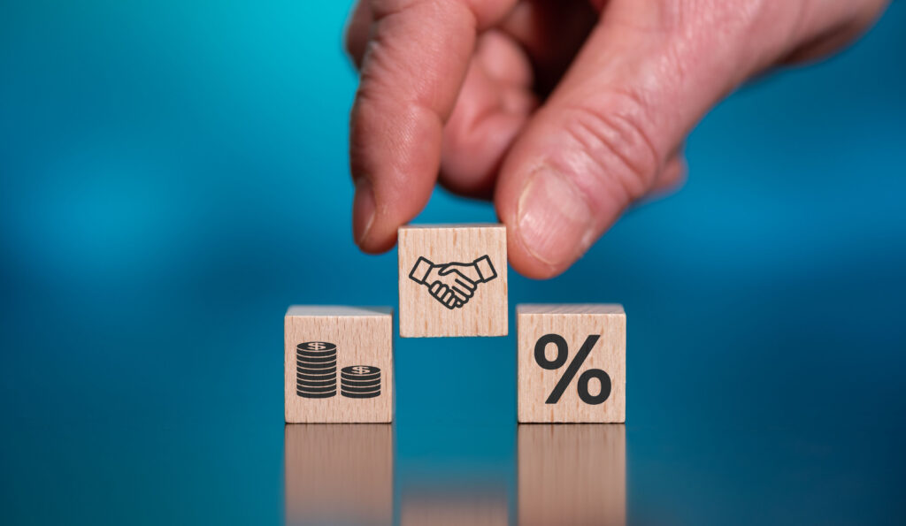 Hand placing a wooden block with a handshake icon between blocks showing money and a percentage symbol.