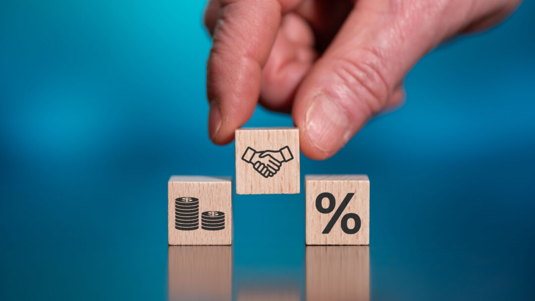 Hand placing a wooden block with a handshake icon between blocks showing money and a percentage symbol.
