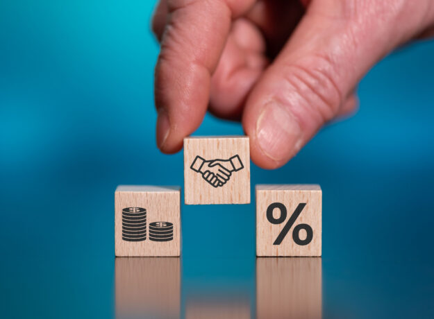 Hand placing a wooden block with a handshake icon between blocks showing money and a percentage symbol.