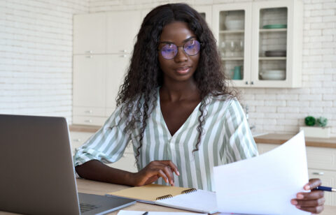 Woman reviewing a document at a table with a laptop and notebook nearby.