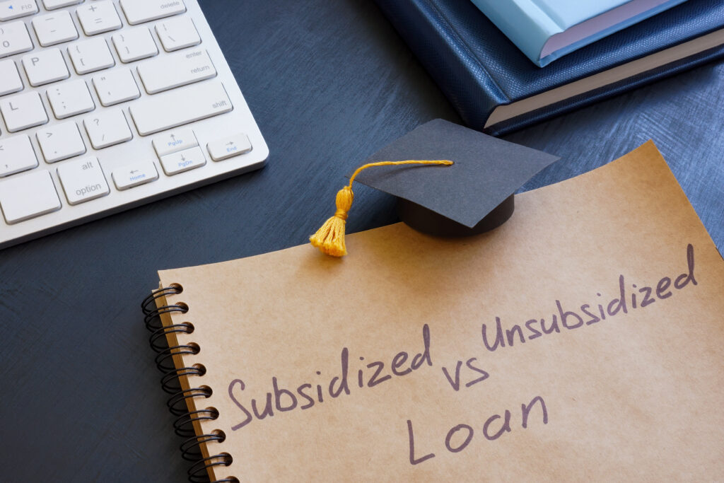 Notebook with the words “Subsidized vs Unsubsidized Loan” written on it, next to a graduation cap and keyboard.