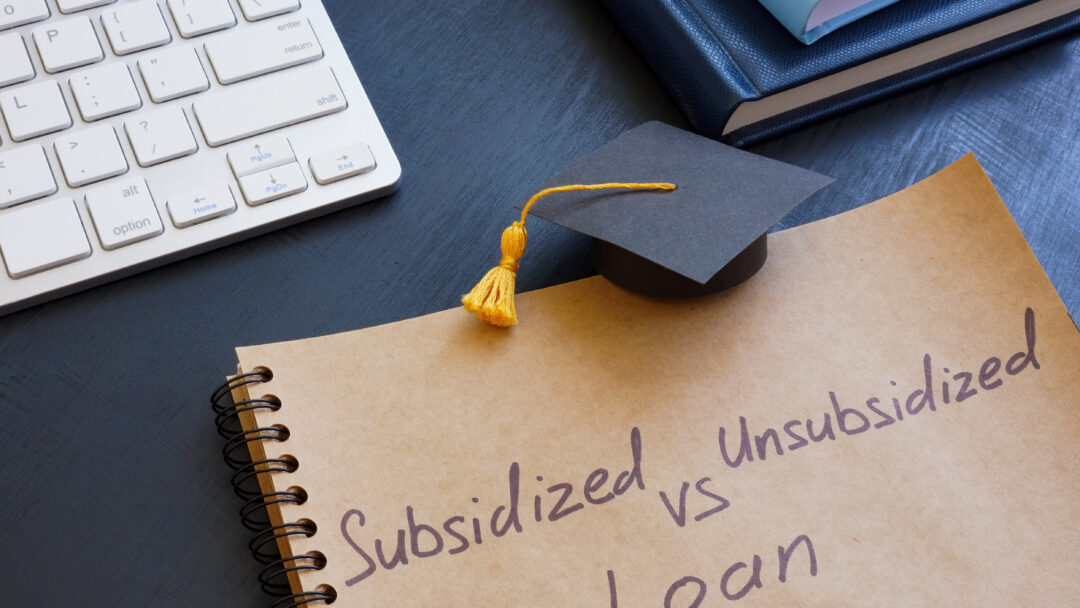 Notebook with the words “Subsidized vs Unsubsidized Loan” written on it, next to a graduation cap and keyboard.