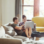 Couple relaxing on a couch at home, looking at a laptop together.