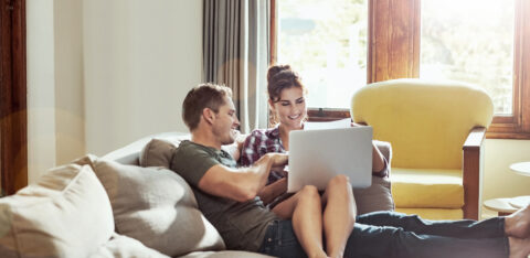 Couple relaxing on a couch at home, looking at a laptop together.
