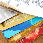 Stack of credit cards with a pen and a receipt showing charges and totals on a wooden surface.