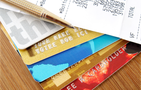 Stack of credit cards with a pen and a receipt showing charges and totals on a wooden surface.