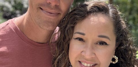 Smiling couple taking a close-up selfie outdoors with trees and sunlight in the background
