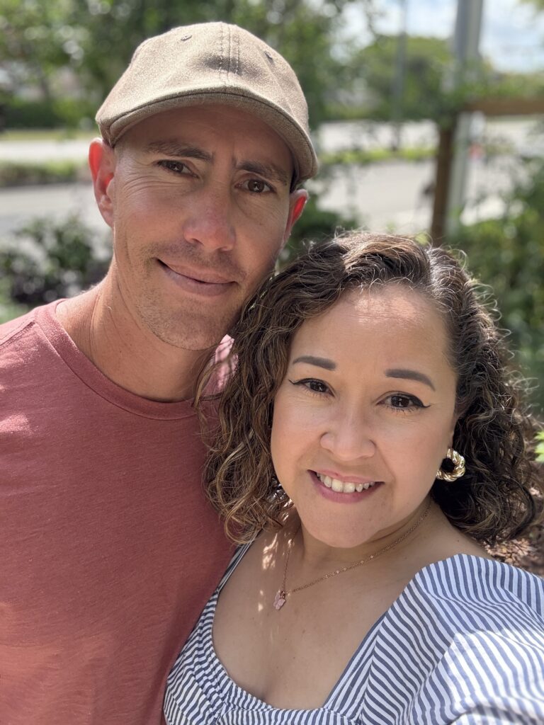 Smiling couple taking a close-up selfie outdoors with trees and sunlight in the background