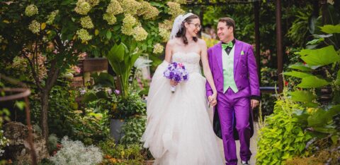Bride and groom walking hand in hand through a garden, smiling at each other.