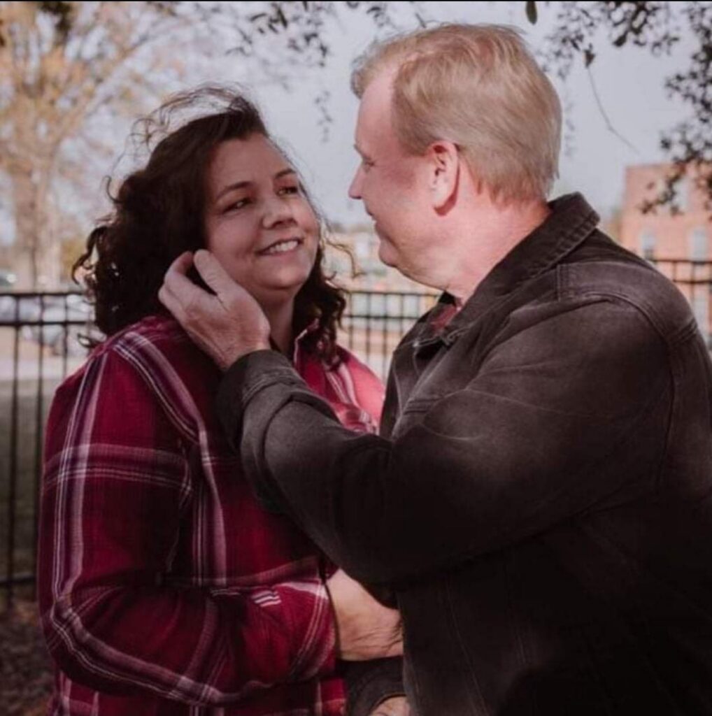 Man and woman sharing a warm moment outside, with the man holding the woman’s cheek as they smile at each other.