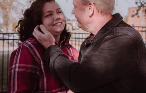Man and woman sharing a warm moment outside, with the man holding the woman’s cheek as they smile at each other.