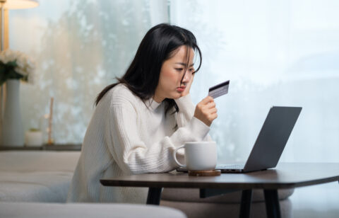 Person sitting at a table using a laptop while holding a credit card, appearing focused