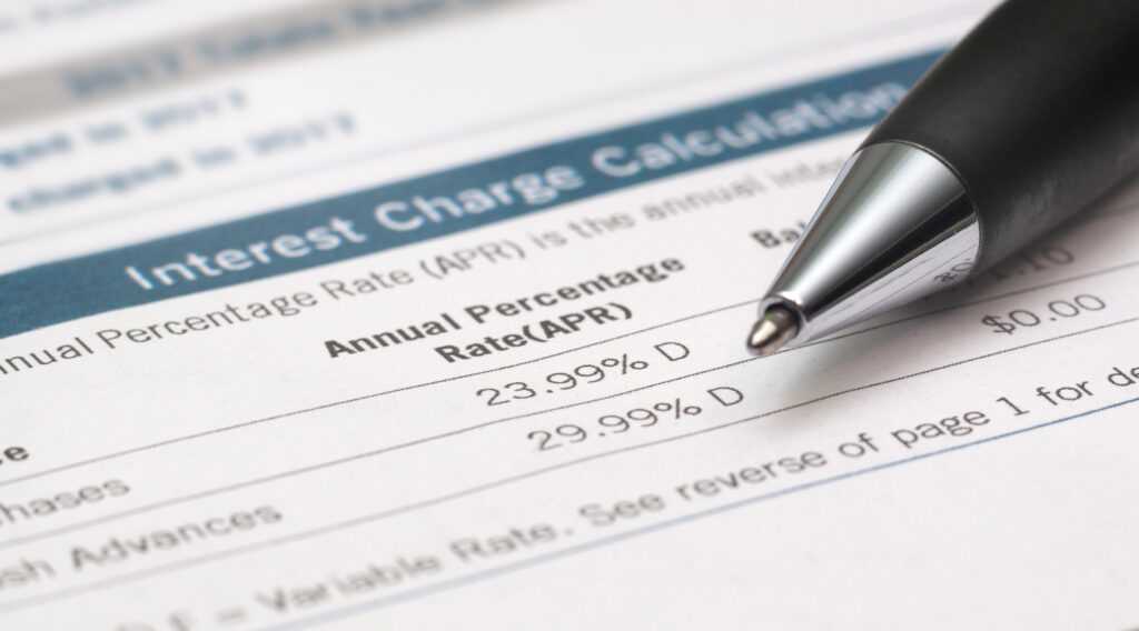 Credit card interest charges document displaying APR rates, with a pen pointing toward the listed percentages.