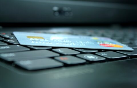 Credit card placed across computer keys, with a blurred laptop screen in the background.