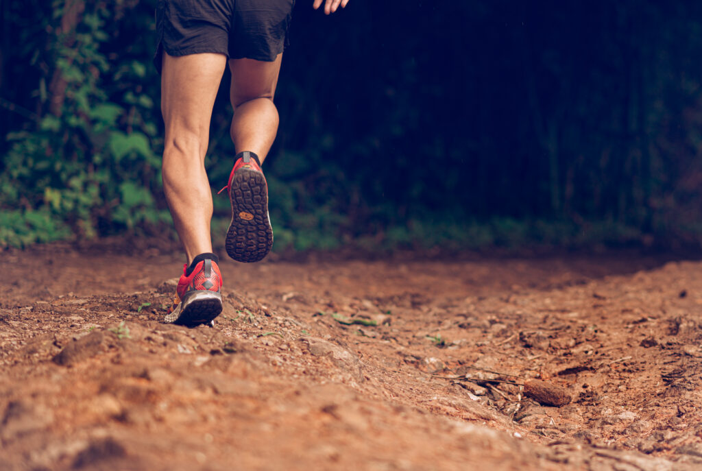 Runner’s legs in motion on a rugged path, moving through a wooded outdoor area