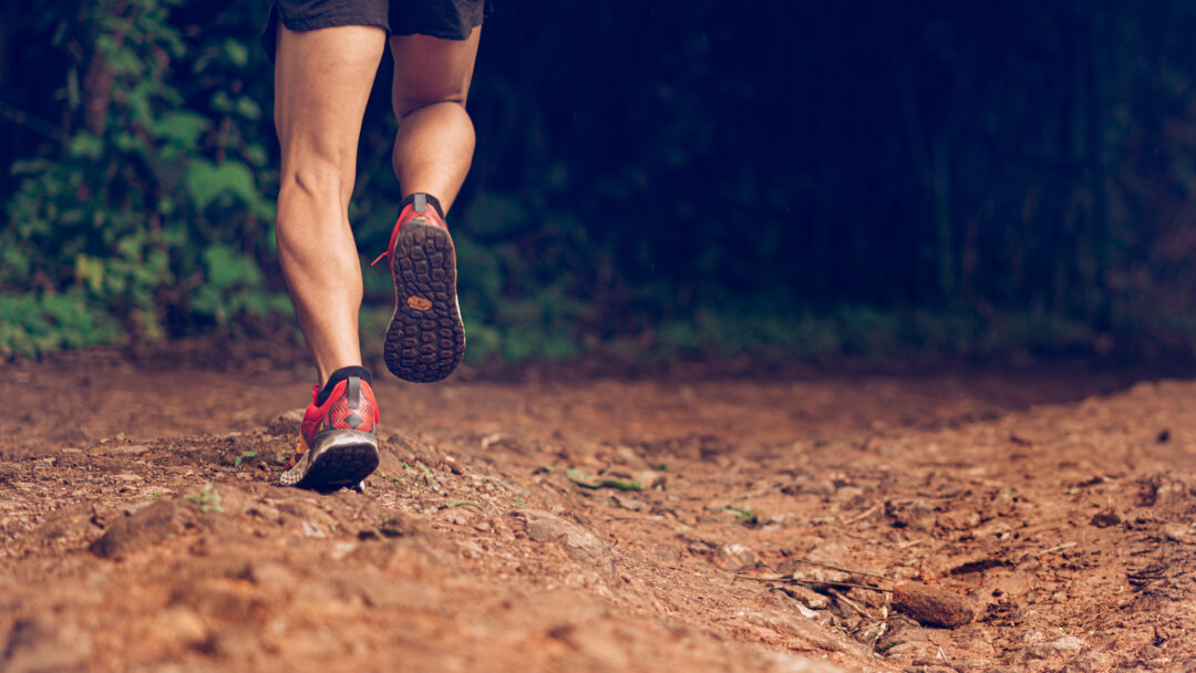 Runner’s legs in motion on a rugged path, moving through a wooded outdoor area