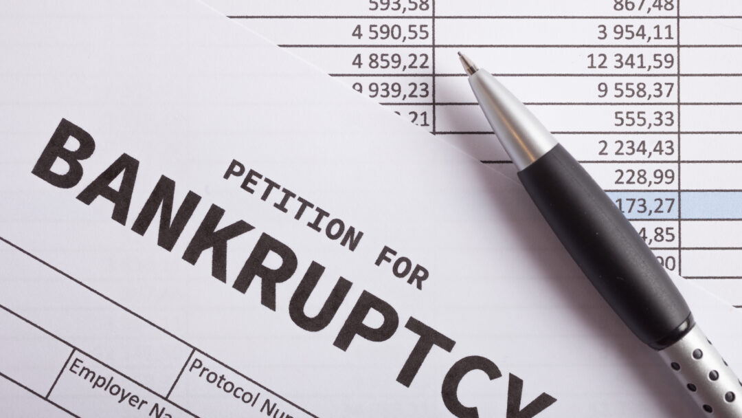 Close-up of a document labeled “petition for bankruptcy” with a pen resting on financial statements